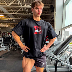 Man in gym wearing black 5% Nutrition t-shirt with red logo and camo shorts, hands on hips