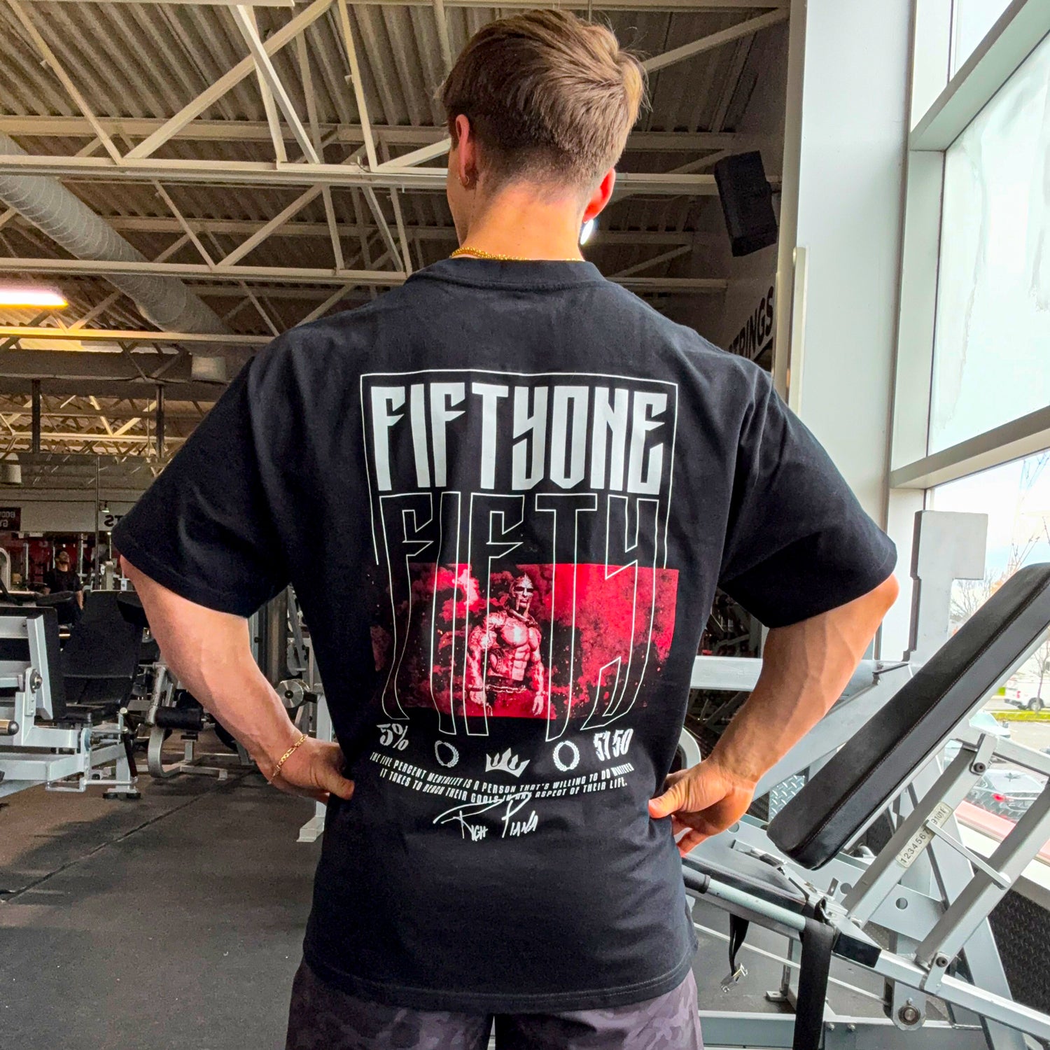 Man wearing black gym t-shirt with 'FIFTHONE FIFTY' graphic, red warrior design, and motivational quote on back.